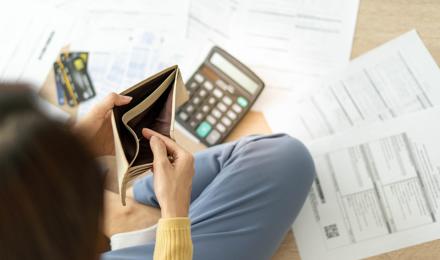 A person is looking inside an empty wallet and has a calculator and paperwork on the floor. They're trying to work out their finances to pay the rent.