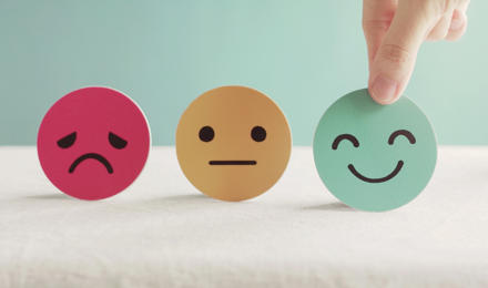 A picture showing a sad, indifferent and happy face. The hand is picking up and choosing the happy face to symbolise their choice to feel happy.