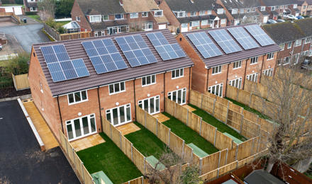 A row of the backs of houses with solar panels on the roof. Each house has its own back garden.