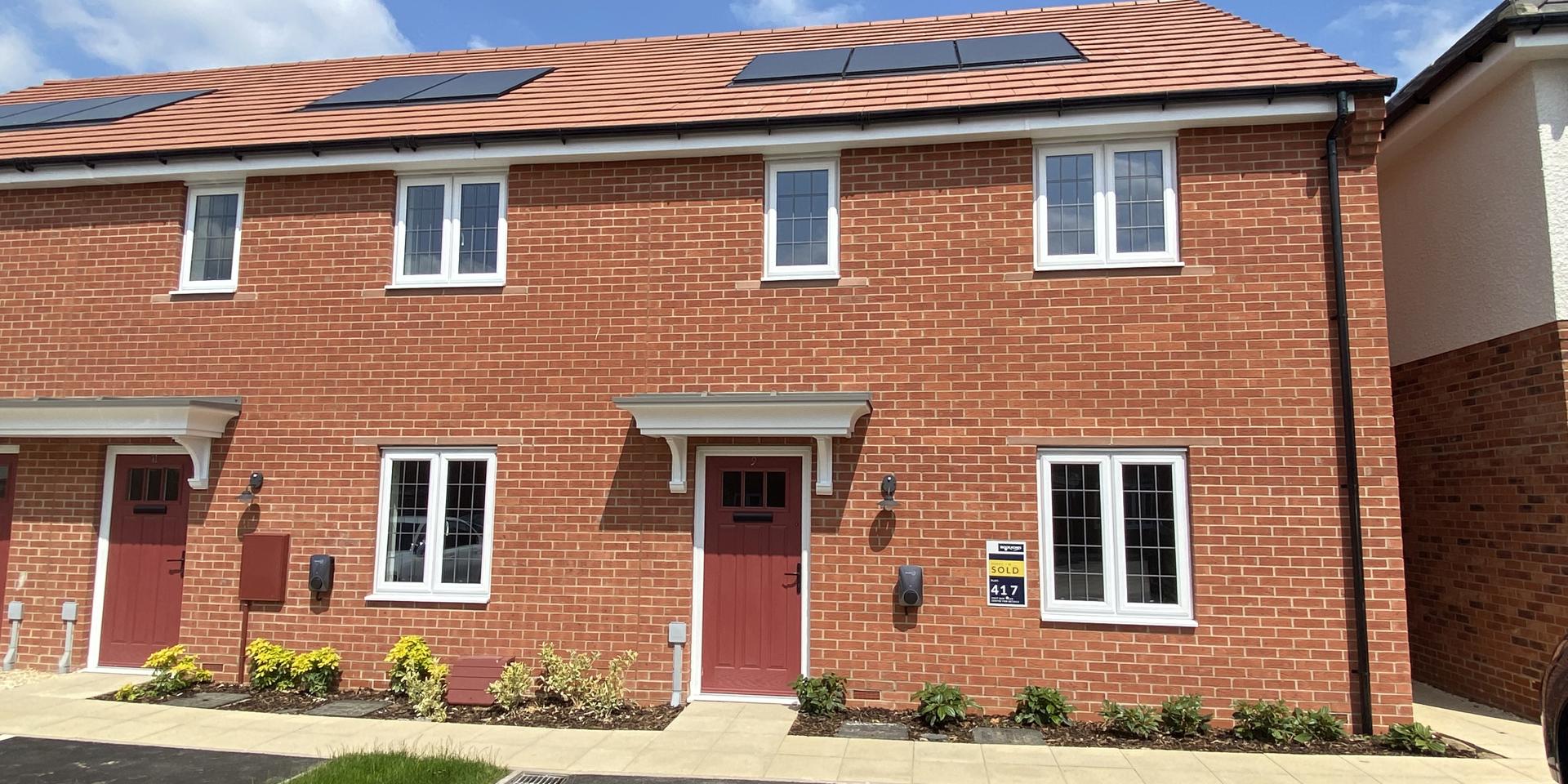 Front view of the property which has a red front door and landscaped planting